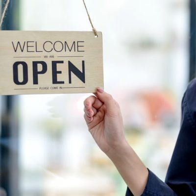 Happy young business owner standing with open sign board. Retail copywriter represented through image of a shop sign